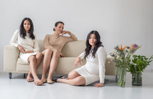 Three models wearing eco friendly organic cotton dresses from slow fashion brand Daniela Salazar. They are smiling, sitting on a sofa. They are wearing the Tana dress in natural colors, brown, ivory and ivory jacquard.