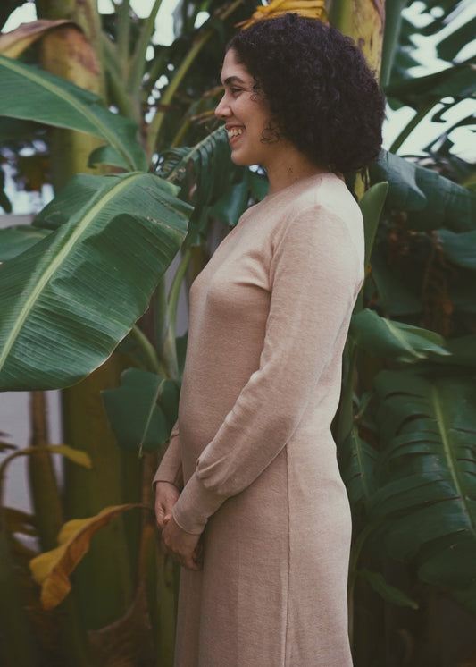 Woman in a light brown dress standing among large green leaves