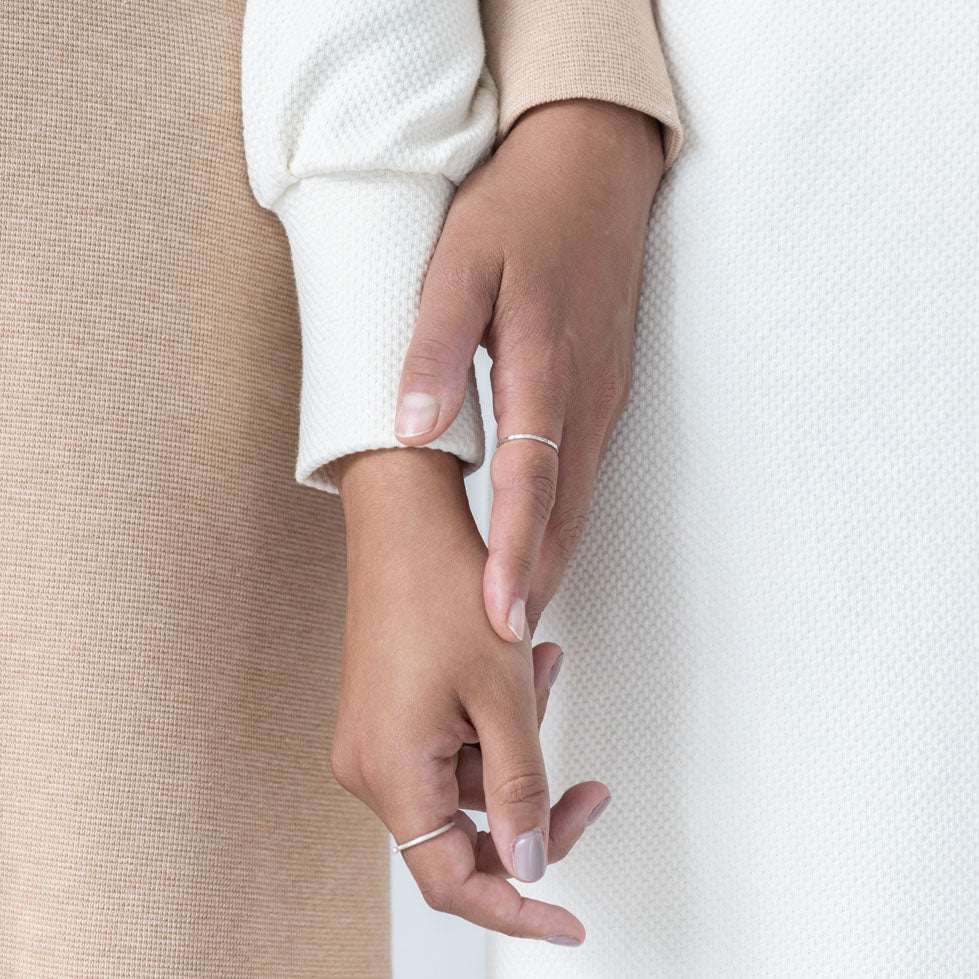 Detail of two hands touching. One woman is wearing a white organic cotton dress, the other woman is wearing a natural colors brown dress. Focus on the textures of the organic cotton jersey fabric.