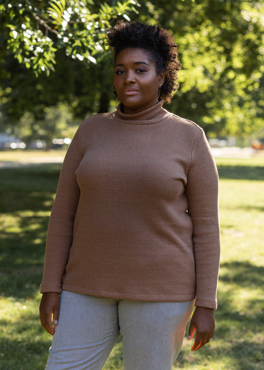 Woman wearing a brown PARK turtleneck sweater and grey CECIL pants. She is standing outdoors with a natural background.