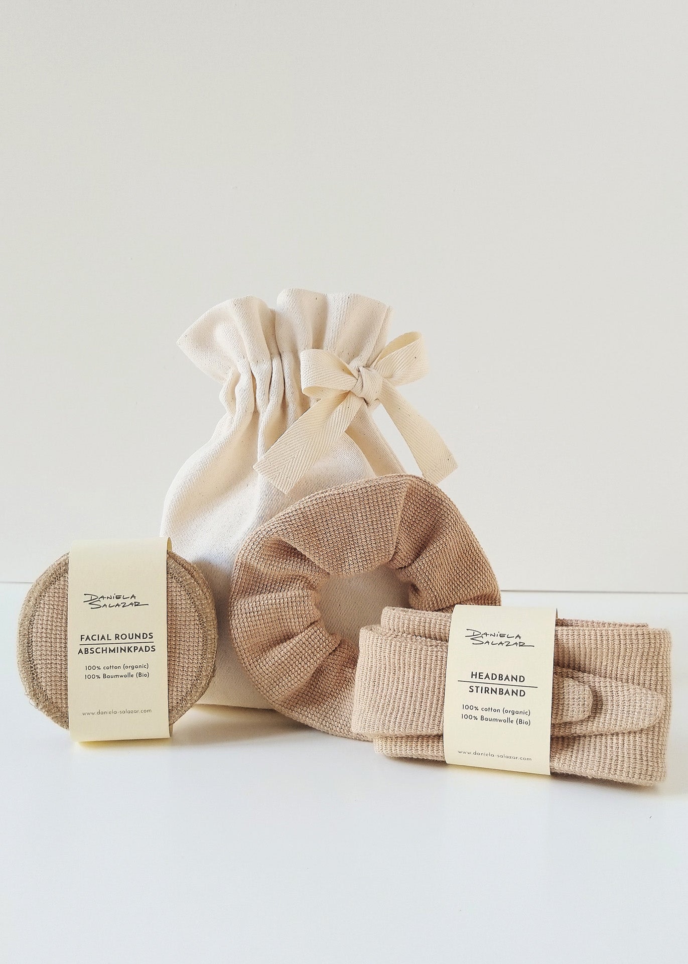 A set of brown-colored home spa accessories including a headband, reusable face pads and a scrunchie, packaged in an ivory gift-ready pouch.