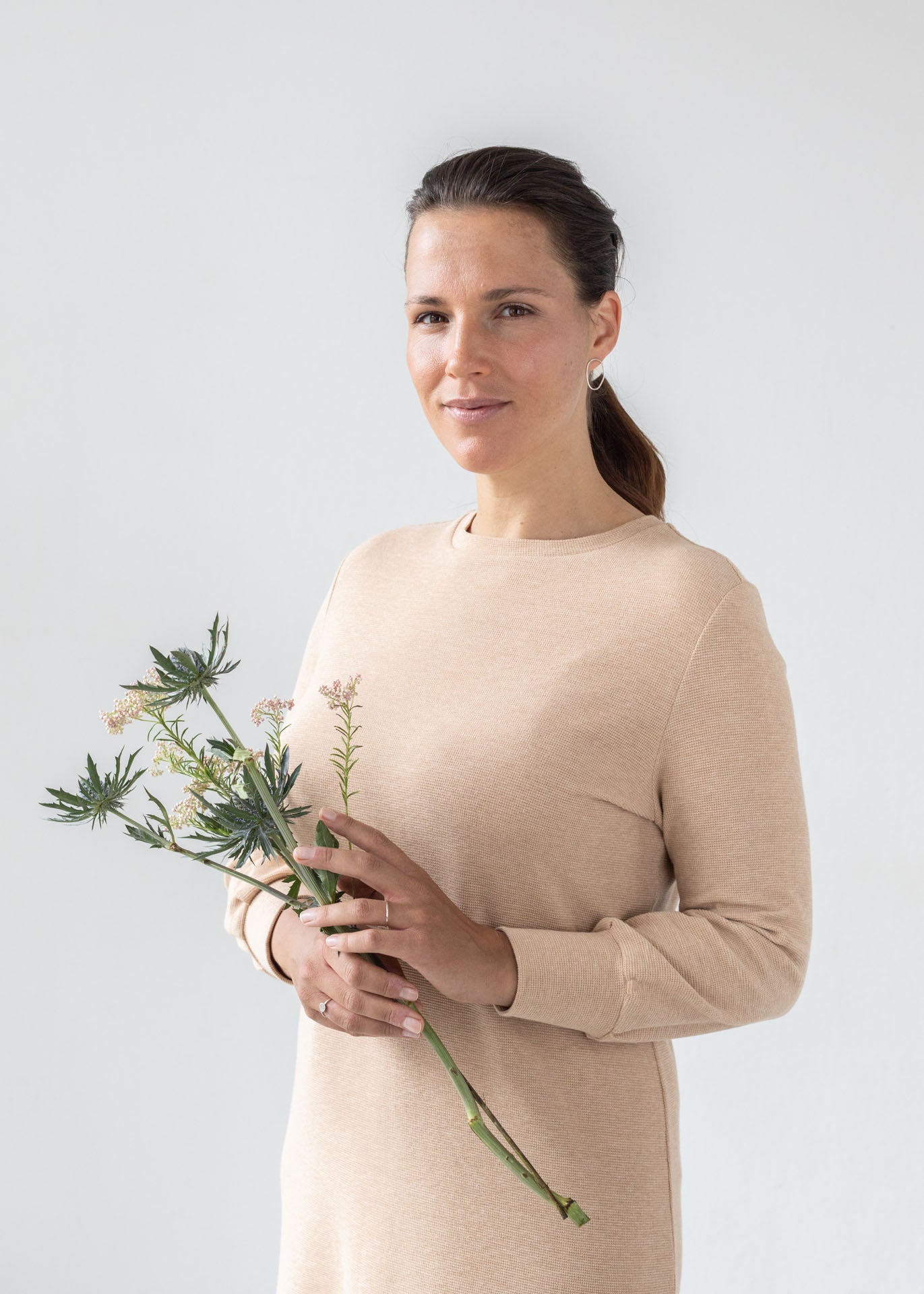woman wearing the eco friendly dress Tana made in Brown Organic Cotton. She is holding a wildflowers bouquet and smiling