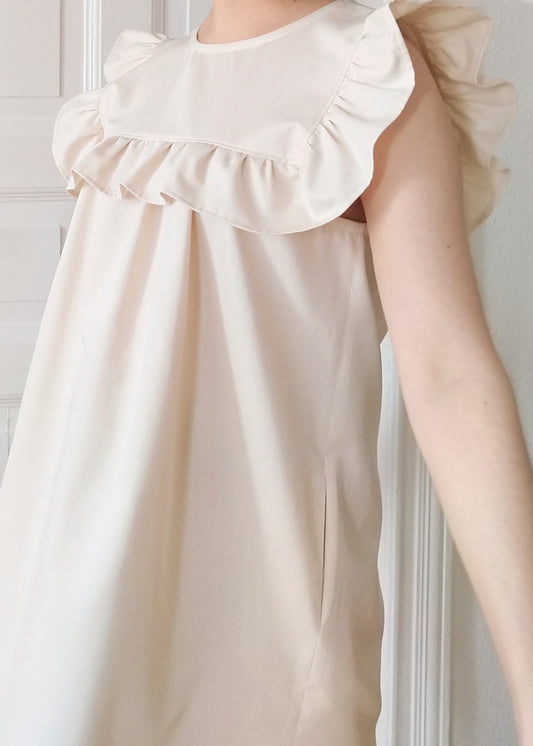 Side detail of the Hana dress in Ecru organic cotton. With its Side seam pockets and Ruffled bib detail.