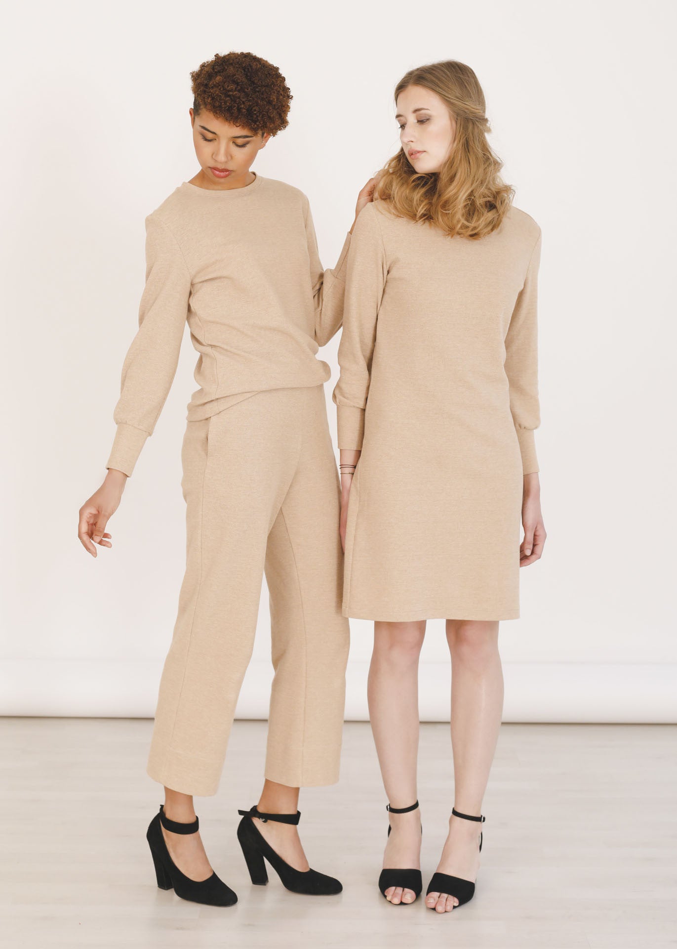 Two women standing together wearing organic cotton clothing in light brown styled with black high heels.