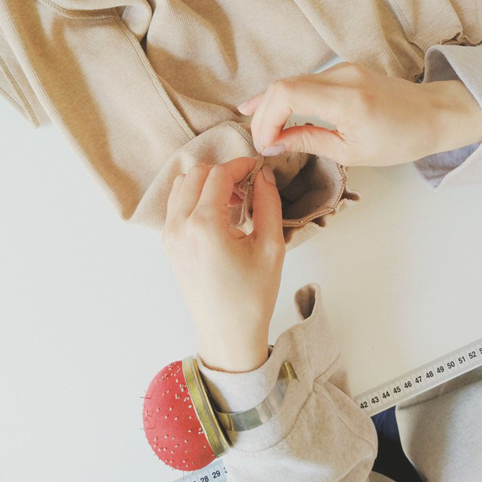 The process of handmade Made-to-order clothing. Detail of two hands pinning organic cotton clothing. On her left hand a red wrist-held pin cushion.