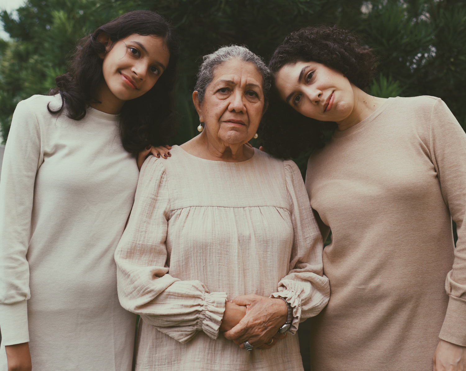 Three generations of women posing outdoors with trees in the background.