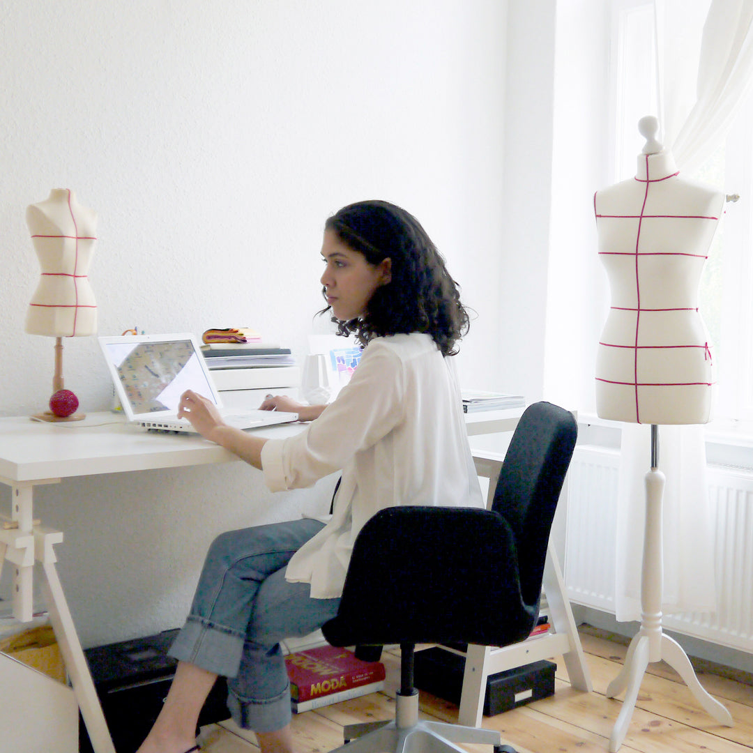 Woman sitting at a desk with a laptop, surrounded by mannequins in a room.