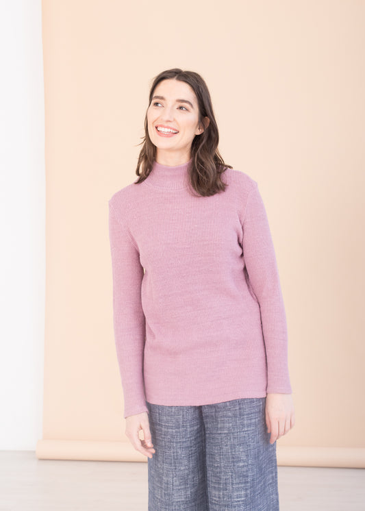 Woman wearing a pink PARK turtleneck sweater and blue TRIADIC pants against a beige background. 
