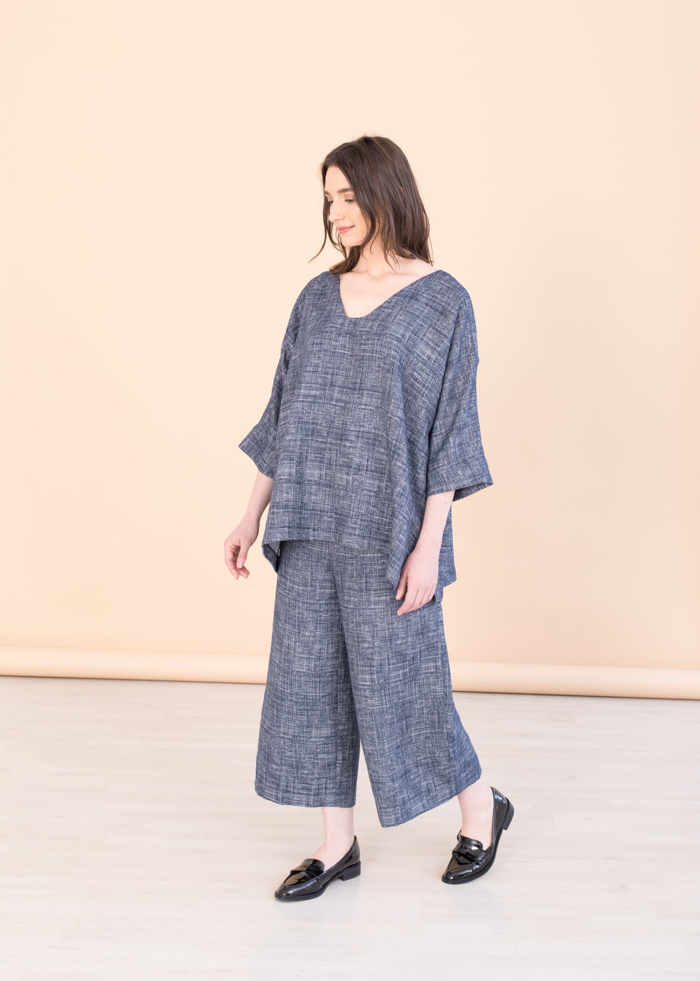 Woman standing against a beige background, wearing a Valentina Tunic Top and Triadic Pants in navy blue.